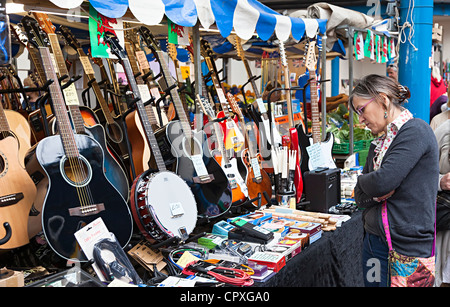 Frau betrachten Gitarren und Musikinstrumente zum Verkauf auf Marktstand, Abergavenny, Wales, UK