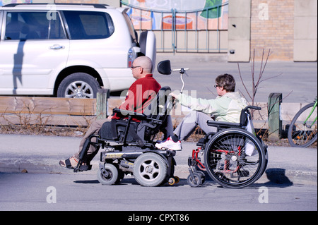 Paar im Rollstuhl in einer Straße der Innenstadt von Montreal. Die Frau Stuhl ist hinter durch des Mannes gezogen, was motorisiert ist. Stockfoto