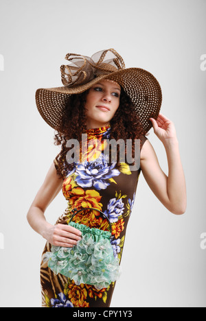 Eine geschweifte junge Frau steht und hält ein Fadenkreuz. Sie trägt eine bunte Sommerkleid und breitkrempigen Hut. Stockfoto