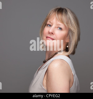 Kopf geschossen Seite auf Porträt von attraktiven lächelnd elegante Reife Frau auf grauem Hintergrund Stockfoto