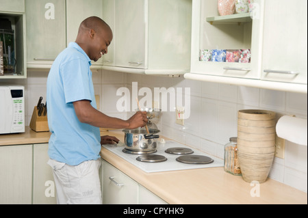 Junge afrikanische Mann stehend auf einem Herd in der Küche Stockfoto