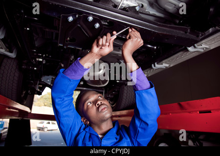 Afrikanischen Mechaniker stehen unter einem Auto, arbeiten am Motor Stockfoto