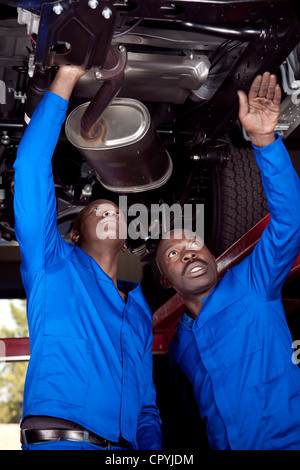 Zwei afrikanische Mechaniker stehen unter einem Auto, arbeiten am Motor Stockfoto