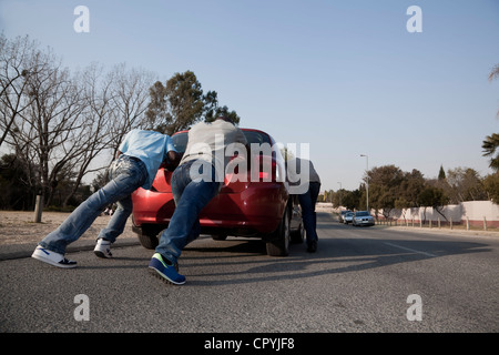 Zwei Männer, ein Auto zu schieben, während ein Drittel es lenkt Stockfoto