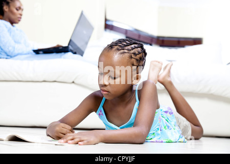 Junge afrikanische Mädchen Färbung mit ihrer Mutter auf einem Laptop im Hintergrund arbeiten Stockfoto