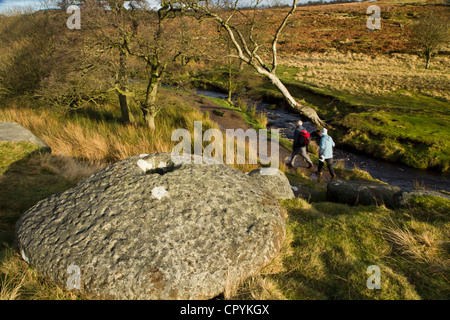 zwei Menschen, die zu Fuß neben Fluss mit Mühlstein im Vordergrund in Derbyshire Peak District England liegend Stockfoto