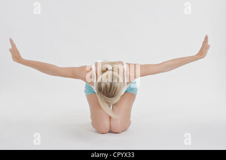 Junge Frau trägt Sportbekleidung kniend auf dem Boden, nach vorne lehnen und streckte ihre Arme zur Seite Stockfoto
