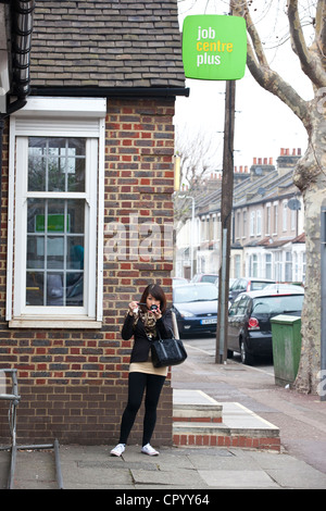 Eine junge Frau macht sich ansehnlich vor dem Eintritt in den Job Centre Plus Büros in Barking, East London, UK. Stockfoto