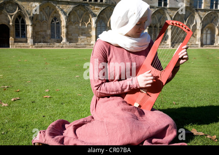 VEREINIGTES KÖNIGREICH. England. Battle Abbey. East Sussex. Frau in mittelalterlichen Kostümen auf Rasen draußen sitzen. spielen traditionelle musikalische inst Stockfoto