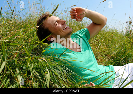 Junger Mann liegend in hohe Gräser, lächelnd, Sonnenbaden Stockfoto