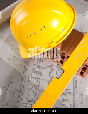 Schutzhelm, Wasserwaage und ein Backstein auf einen Bauplan Stockfoto