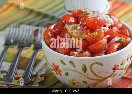 Eine dekorative Schüssel Tomaten-Feta-Käse-Salat mit 3 Gabeln auf eine bunte, gestreifte Tischdecke. Stockfoto