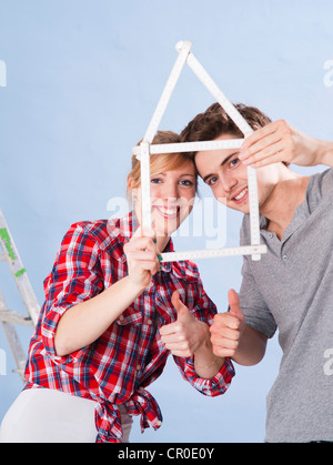 Junges Paar hält eine Faltung des Tischlers Herrscher in der Form eines Hauses Stockfoto