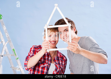 Junges Paar hält eine Faltung des Tischlers Herrscher in der Form eines Hauses Stockfoto