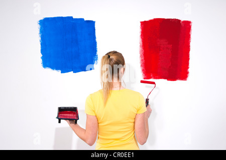 Junge Frau mit einer Farbwanne und ein Farbroller vor einer Wand mit Farbproben Stockfoto