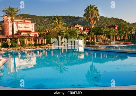 Sweeming Pool mit blauem Wasser in der Nähe von Gebäuden, umgeben von Palmen, Liegestühlen und Sonnenschirmen Stockfoto