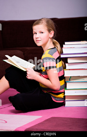 Mädchen, 11, lehnte sich gegen einen Stapel Bücher Stockfoto