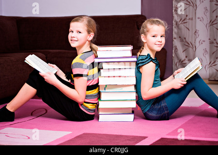 Mädchen, 11 und 8, lehnte sich gegen einen Stapel Bücher Stockfoto