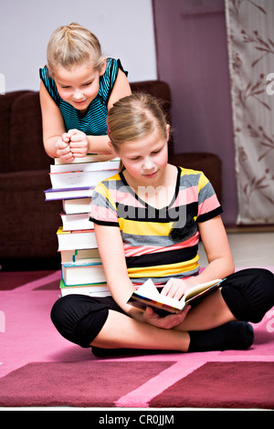 Mädchen, 11 und 8, lehnte sich gegen einen Stapel Bücher Stockfoto