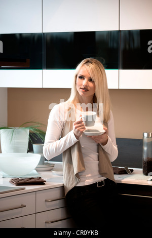 Junge Frau mit Kaffeetasse in der Küche Stockfoto