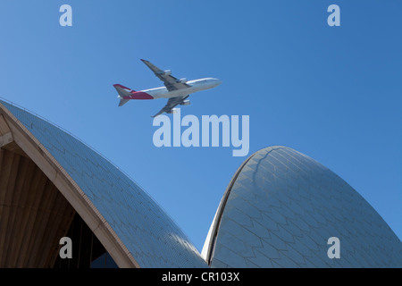 Eine Ansicht des Sydney Opera House gegen ein strahlend blauer Himmel mit einem Flugzeug fliegen geringem Overhead. Stockfoto