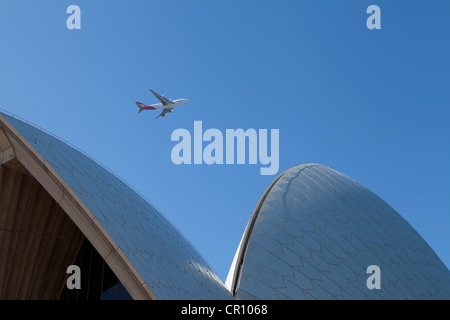 Eine Ansicht des Sydney Opera House gegen ein strahlend blauer Himmel mit einem Flugzeug fliegen geringem Overhead. Stockfoto