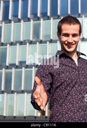 junger Student gibt Handschlag gegen Schule Gebäude Einladung zur Zusammenarbeit Stockfoto