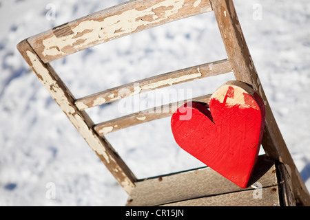 Rotes Herz aus Holz auf einem alten Stuhl im Schnee Stockfoto