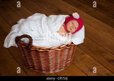 Neugeborenes Babymädchen, zwei Wochen alt, mit roten Käppchen, liegend in einem Korb Stockfoto