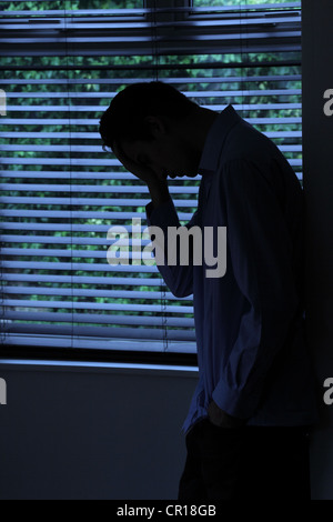 Silhouette des jungen männlichen lehnt gegen eine Wand durch ein Fenster. Stockfoto