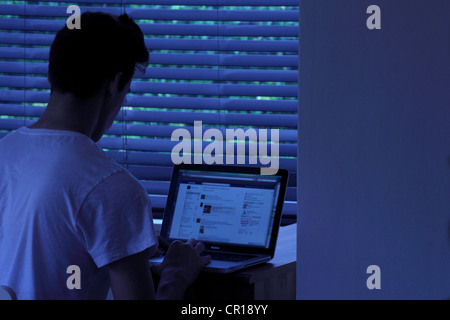 Junger Mann in einem dunklen Raum mit einem Laptop sitzt. Stockfoto
