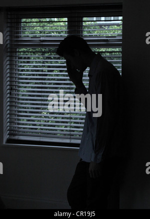 Silhouette eines männlichen stehenden in einem dunklen Raum mit Licht aus einem Fenster mit Jalousien, seine Gestalt, Hand, Gesicht zu zeigen. Stockfoto