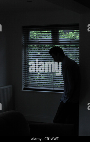 Silhouette eines männlichen stehenden in einem dunklen Raum mit Licht aus einem Fenster mit Jalousien zeigt seine Gestalt. Stockfoto