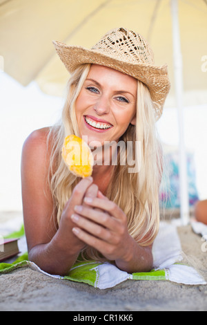 Lächelnde Frau essen Eis am Stiel am Strand Stockfoto