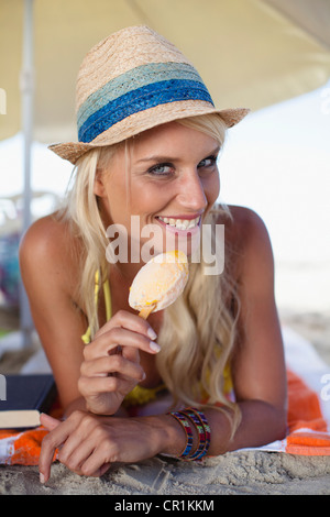 Lächelnde Frau essen Eis am Stiel am Strand Stockfoto
