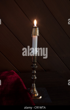 Weiße Kerze Kerze beleuchtet auf Basis mit dunklem Holz und rotem Stoff daneben in vertikalen gold Kerzenhalter. Stockfoto