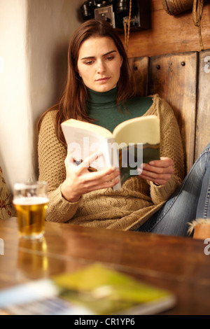 Frau liest mit Bier in der Kneipe Stockfoto