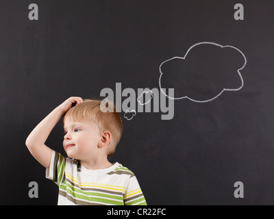 Niedlichen Kleinkind Jungen (2-3) kratzte sich am Kopf gegen die Tafel mit Kreide geschrieben Gedankenblase Stockfoto