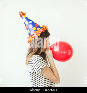 Studioaufnahme der jungen Frau trägt Partyhut und bläst Ballon Stockfoto