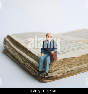 Älterer Mann, Miniatur Figur sitzt auf einem alten Buch. Stockfoto