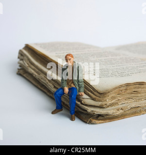 Junger Mann / Student Miniatur Figur, sitzt auf einem alten Buch - Universität / Ausbildung / Studium / Lernkonzept. Stockfoto