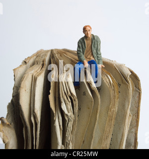 Junger Mann / Student Miniatur Figur, sitzt auf einem alten Buch - Universität / Ausbildung / Studium / Lernkonzept Stockfoto