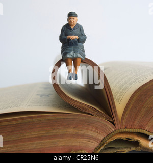 Ältere Dame, Miniatur Figur sitzt auf einem alten Buch - Geschichte-Konzept. Stockfoto