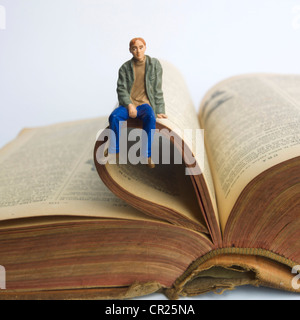 Junger Mann / Student Miniatur Figur, sitzt auf einem alten Buch - Universität / Ausbildung / Studium / Lernkonzept Stockfoto