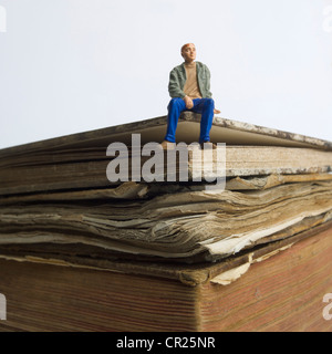 Figurine eines jungen Mannes, der auf einem Buch sitzen Stockfoto