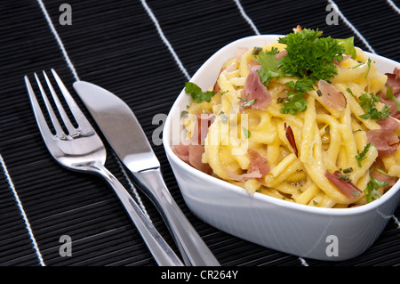 Portion Käse Spätzle in eine Schüssel geben (auf schwarze Tischdecke) Stockfoto