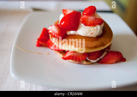 Erdbeeren auf Pfannkuchen mit Creme Fraiche serviert beträufelt für ein gesundes Frühstück mit Honig. Stockfoto