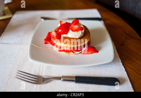 Erdbeeren auf Pfannkuchen mit Creme Fraiche serviert beträufelt für ein gesundes Frühstück mit Honig. Stockfoto