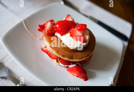 Erdbeeren auf Pfannkuchen mit Creme Fraiche serviert beträufelt für ein gesundes Frühstück mit Honig. Stockfoto