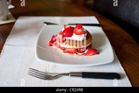 Erdbeeren auf Pfannkuchen mit Creme Fraiche serviert beträufelt für ein gesundes Frühstück mit Honig. Stockfoto